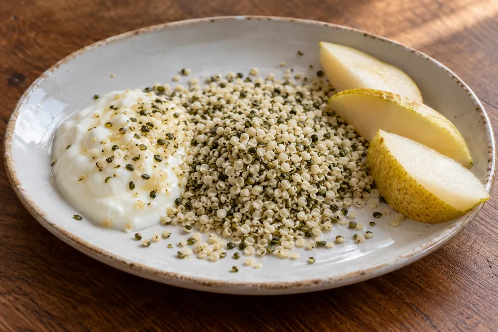 Semillas peladas con yogur y pera sobre un plato.