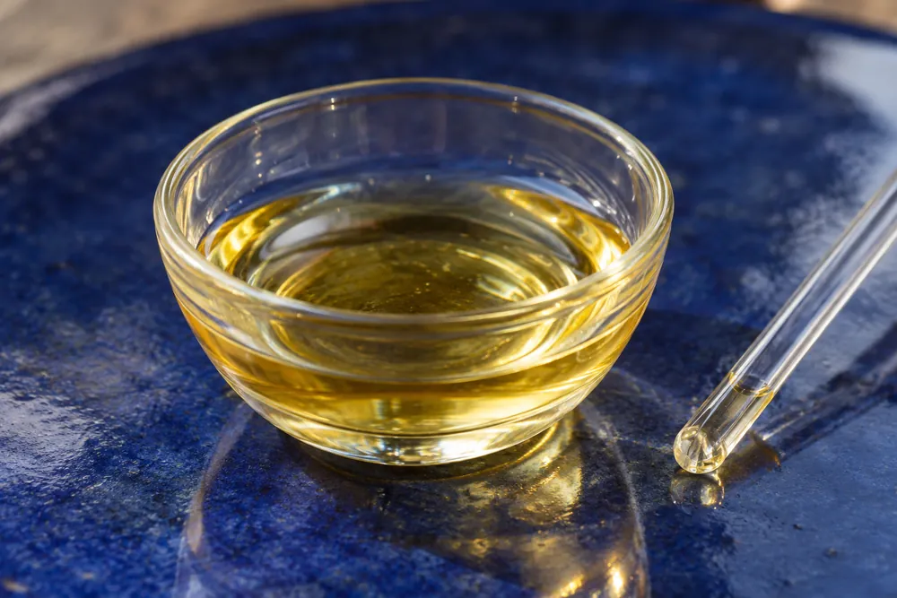 Aceite cosmético en una copa de vidrio sobre cerámica azul.