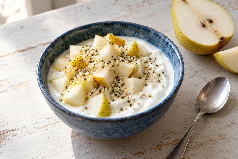 Yogur natural con dados de pera y semillas de cáñamo peladas en un cuenco azul